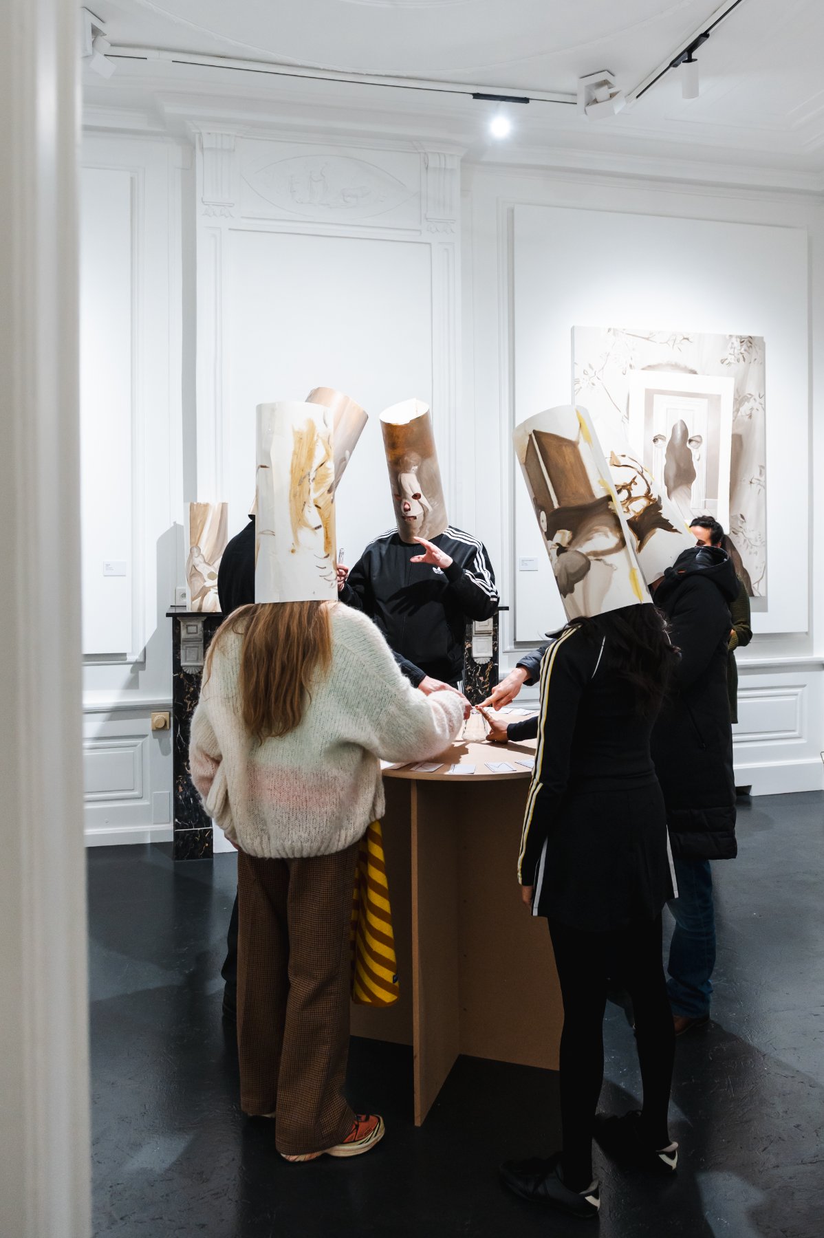 Hell — masked visitors gathered around a small table in the gallery, wearing painted cylinder masks.