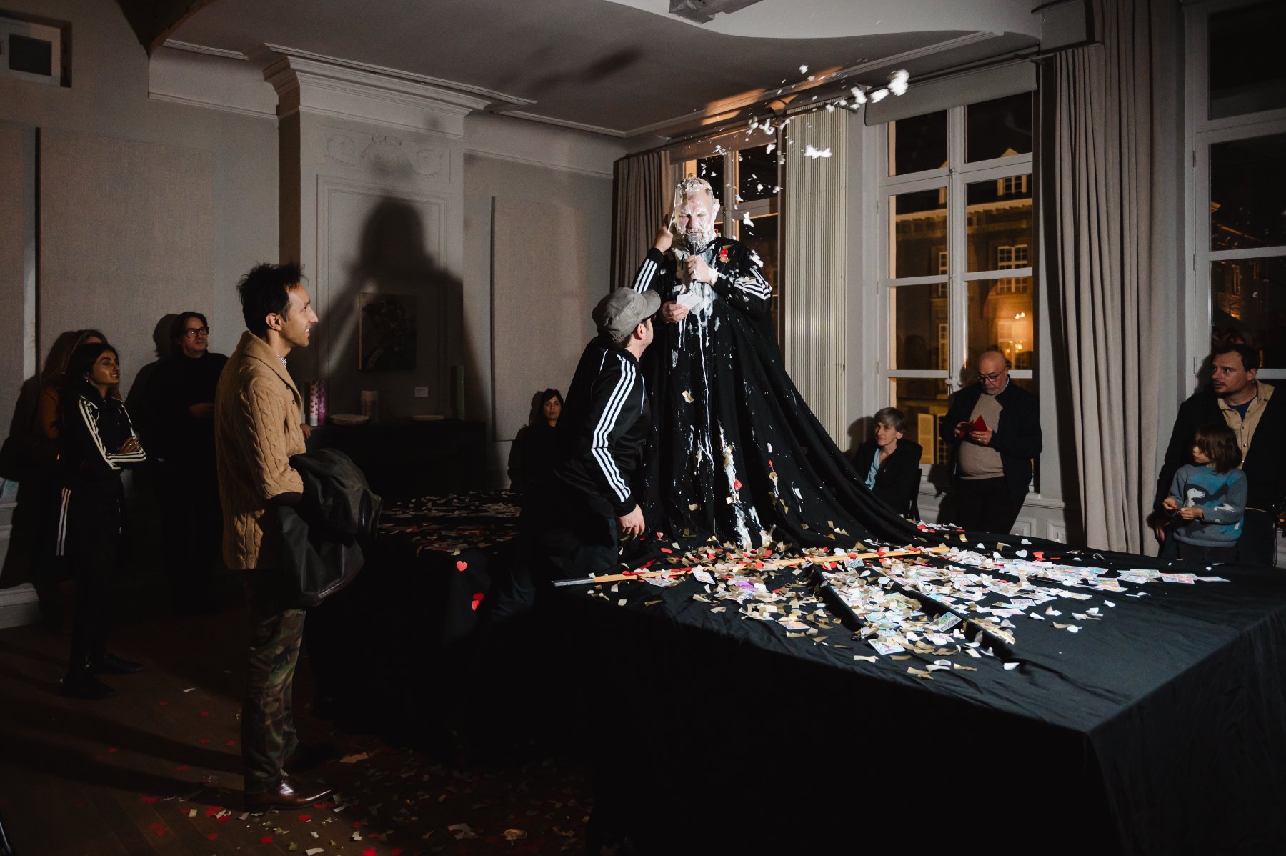 Purgatory — Robinson stands on a black-draped table in a long gown, head covered in cream, as a participant reaches up.