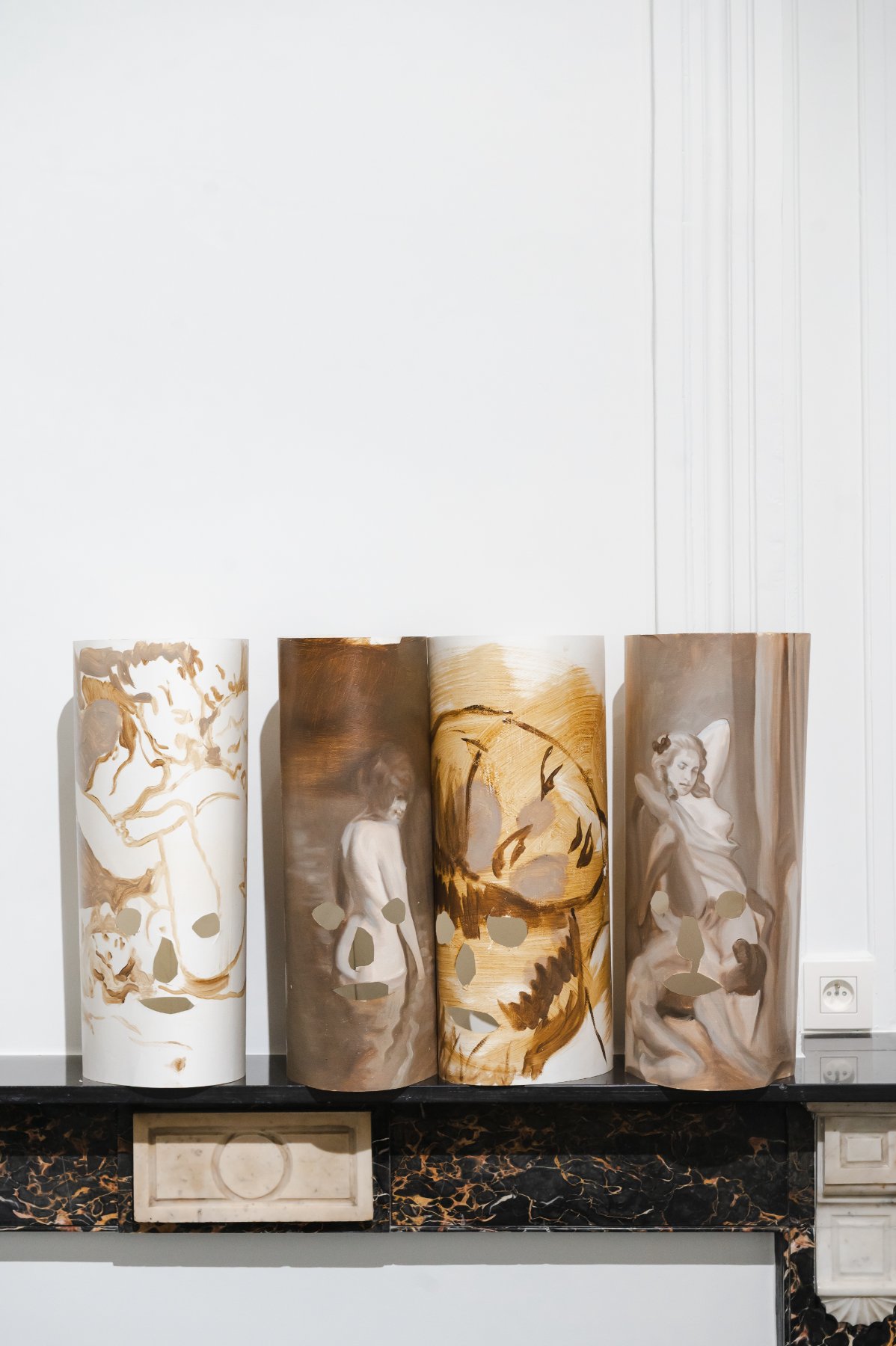 Hell — four painted cylinder masks with cut-out faces standing on a black marble mantelpiece.