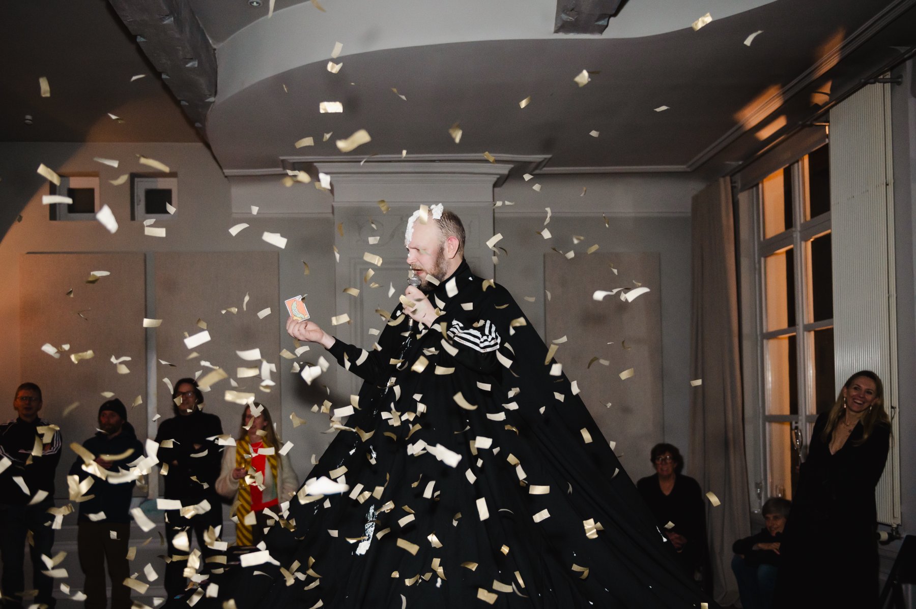 Purgatory — Robinson in a long black gown holding a card and microphone amid falling confetti.