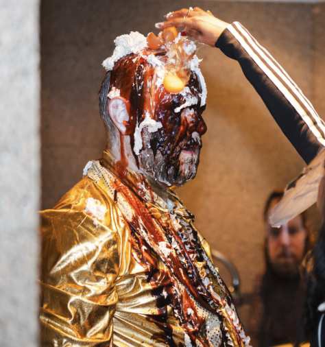 Heaven — a participant pours sauce over Robinson’s head; his gold costume streaked with red and dark liquids.